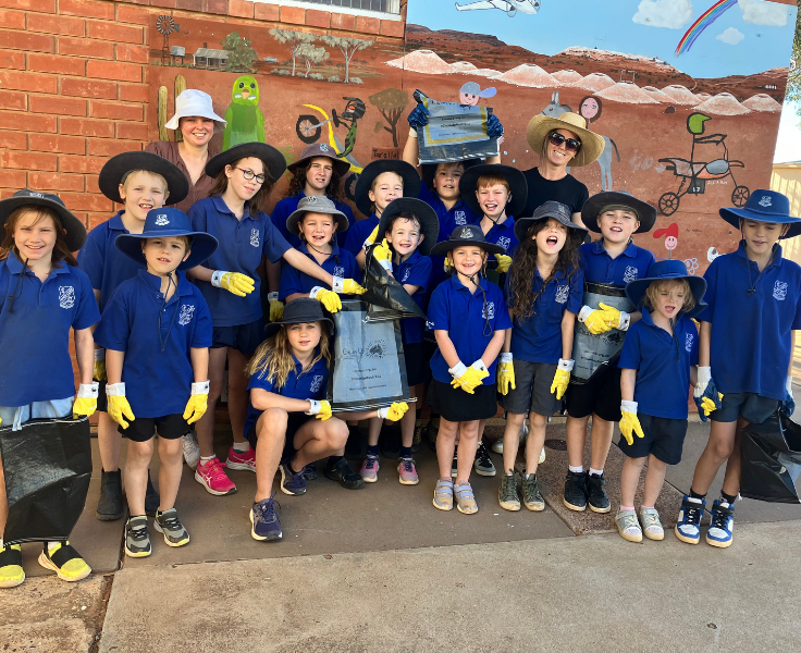 Whole school photo of students in front of Artwork showing off Clean Up Australia Bags and gloves