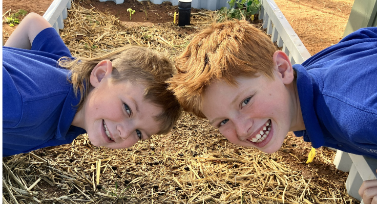 Two students smiling whilst admiring the leaves of a vegetable growing in the school garden