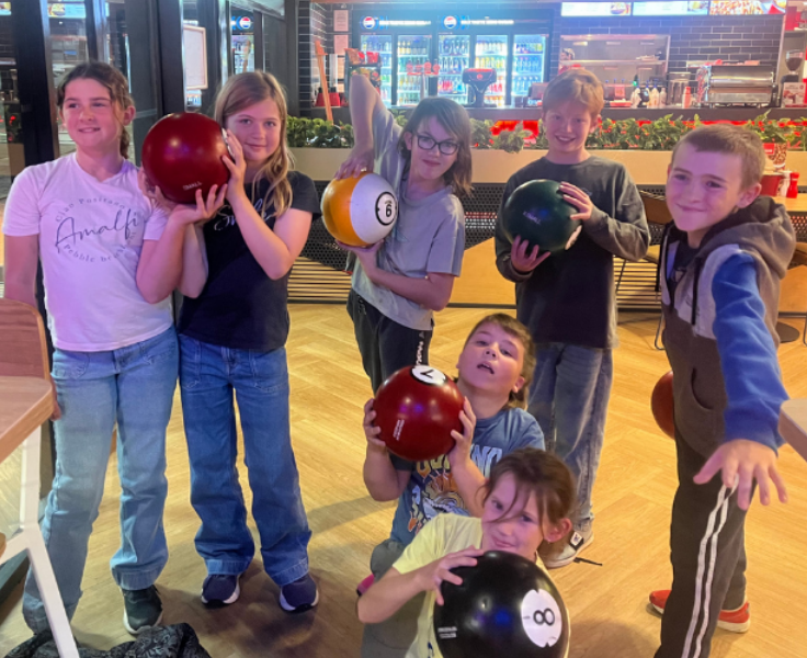 7 students holding up bowling balls and smiling